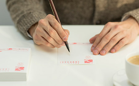 筆ペンではがきの宛名を書く男性