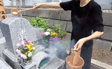 墓石に水をかける喪服の女性
